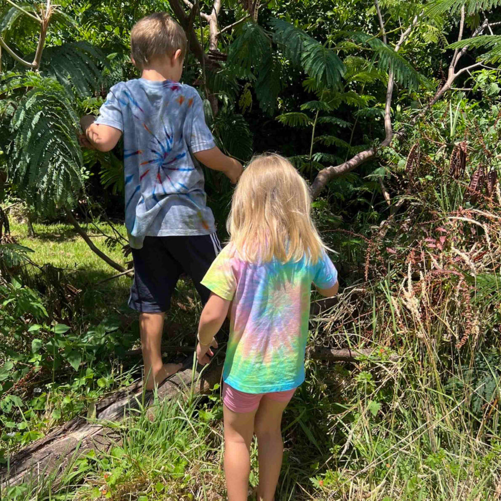 Two children in tie-dye shirts walking through a forest